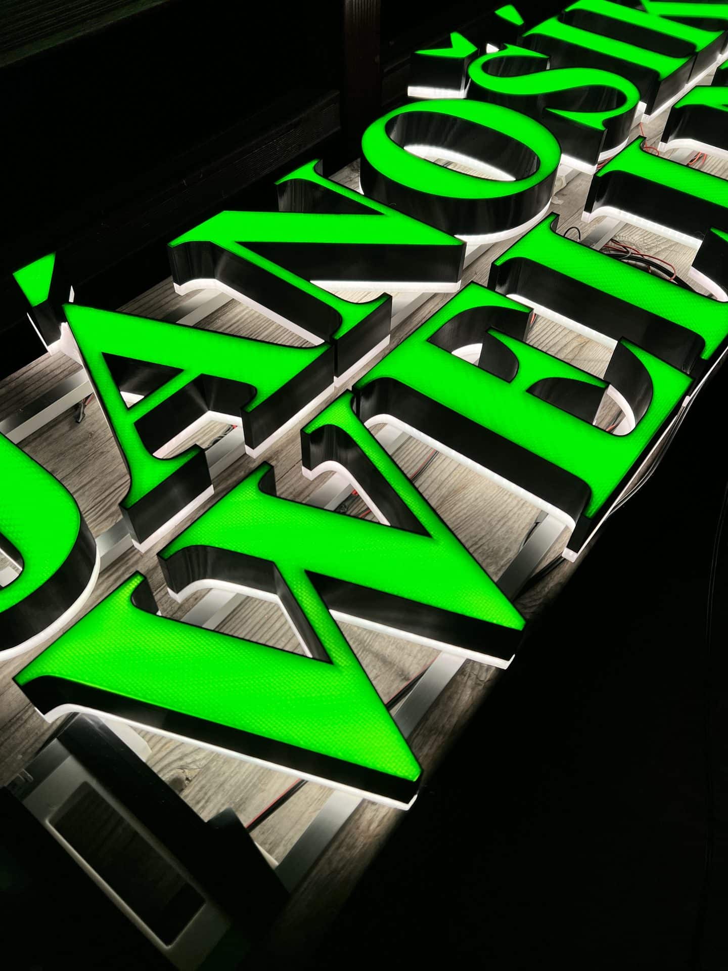 Close-up of glowing green 3D-printed channel letters on a wooden wall
