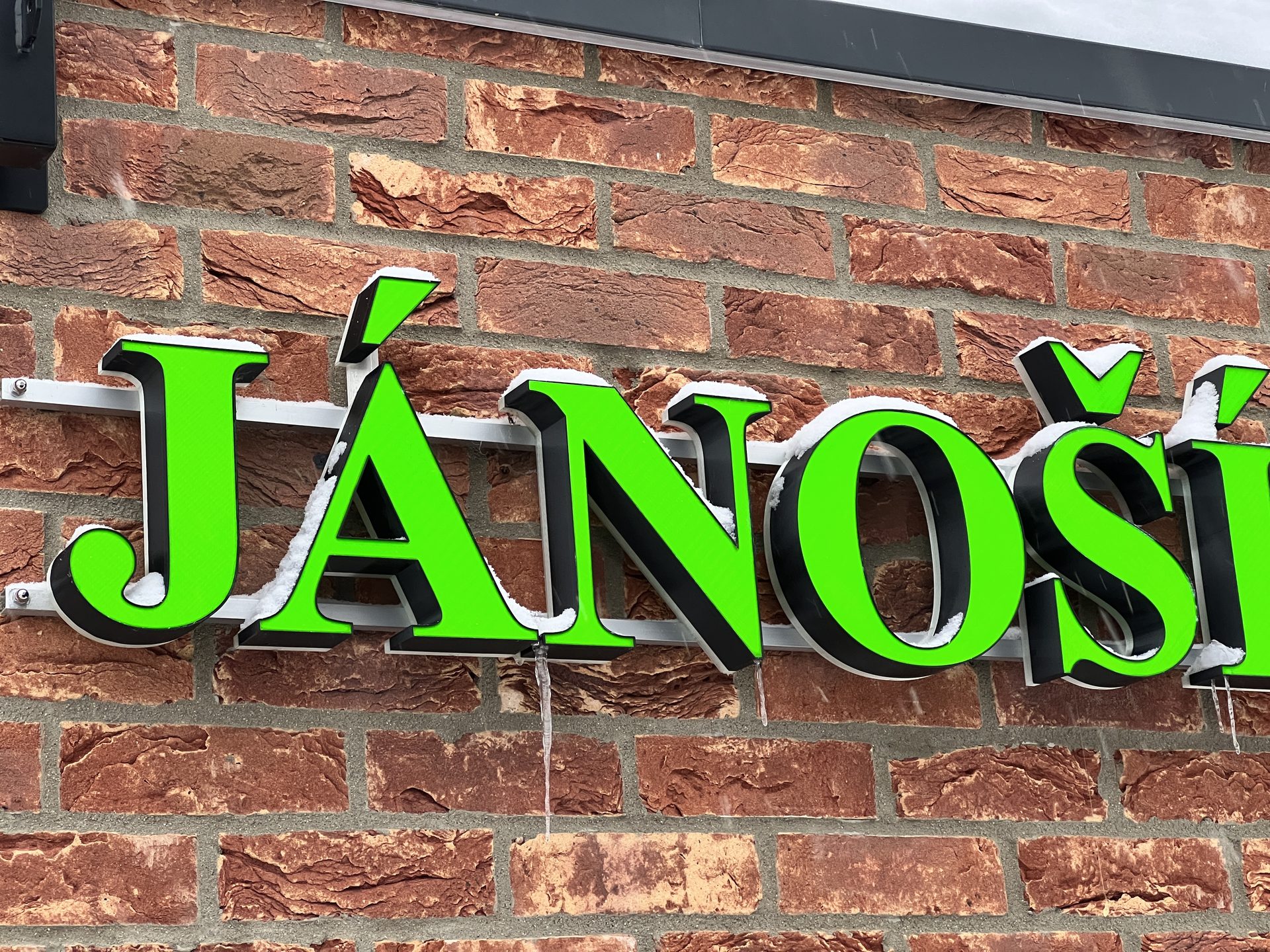 3D-printed channel letters JÁNO on a brick wall in daylight