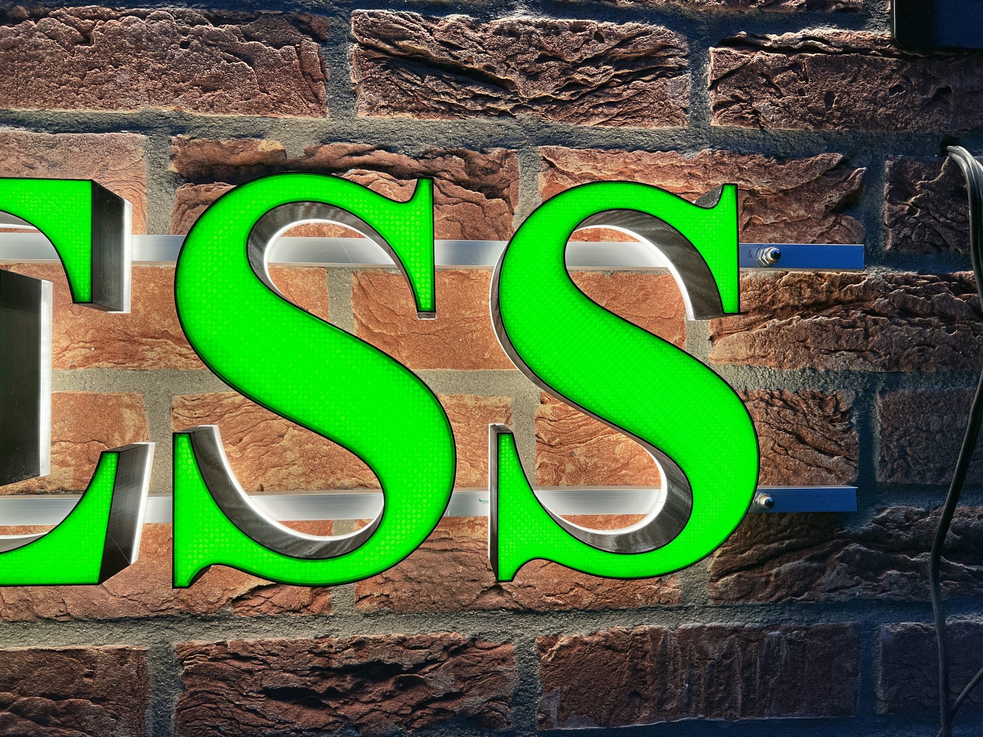 Detail of the letters ESS on a brick wall, lit from inside