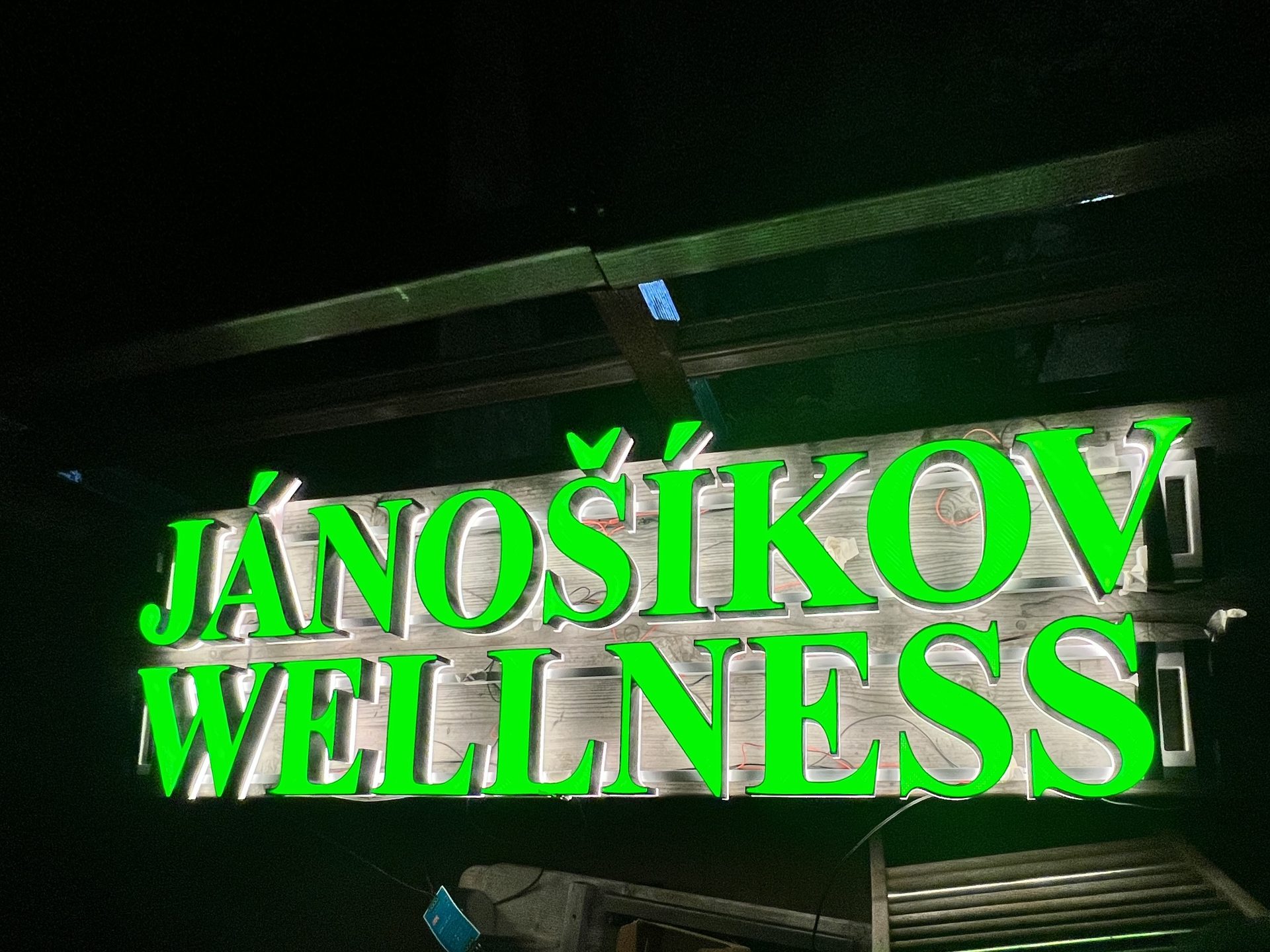 Green illuminated 3D-printed channel letters JÁNOÍKOV WELLNESS at night
